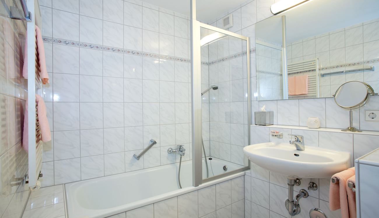Badezimmer im der Zwei-Raum-Ferienwohnung ausgestattet mit Kosmetikspiegel, Dusche & Badewanne. 